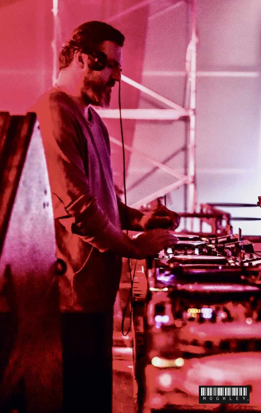 DJ performing on turntables at an outdoor event, red lighting