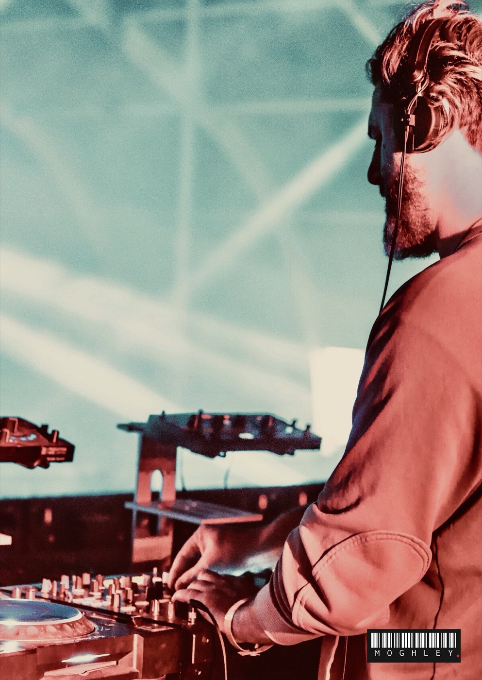 DJ wearing headphones at the decks, teal-toned stage lighting