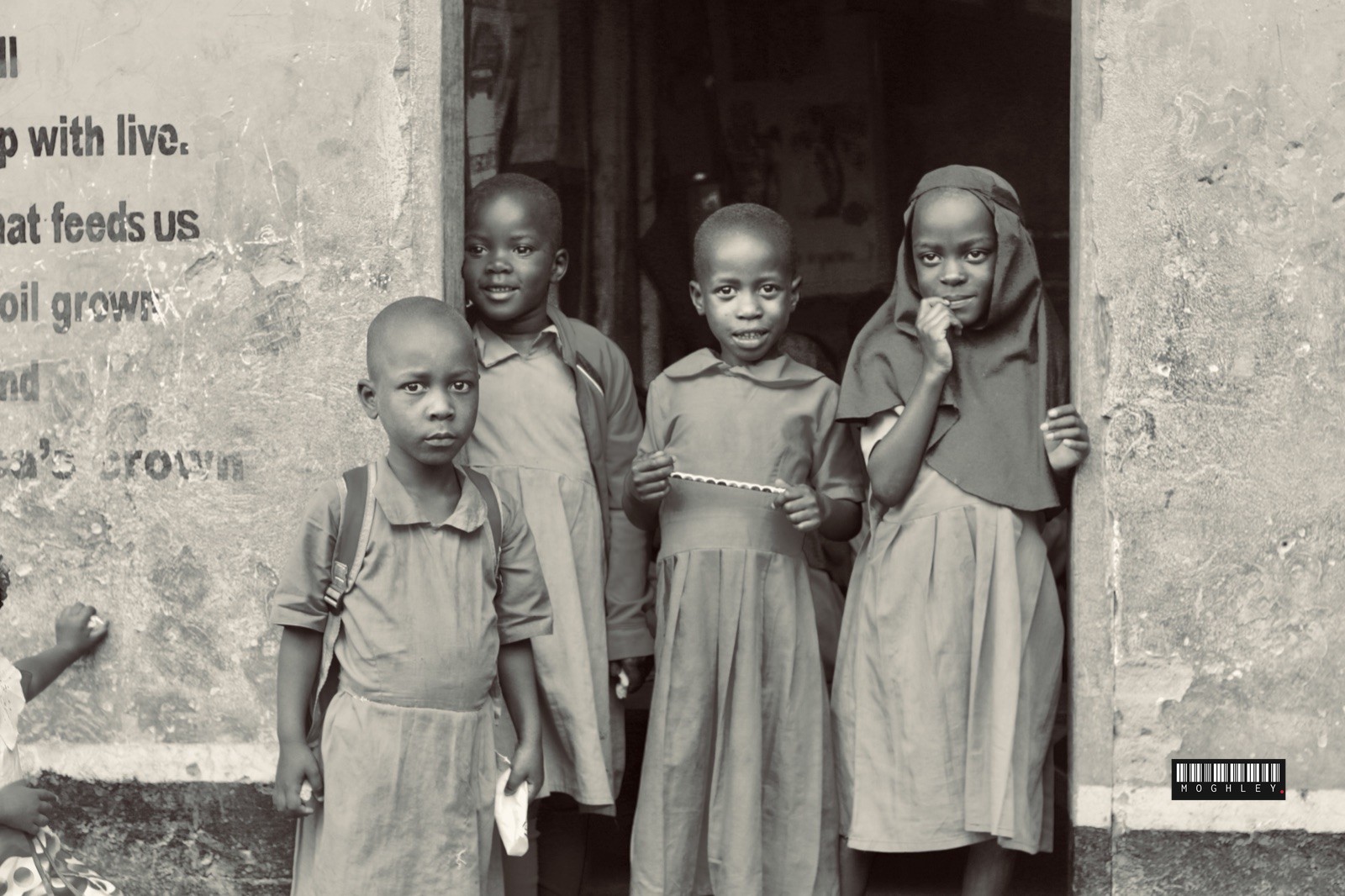 Black and white documentary portrait of four children standing in a doorway