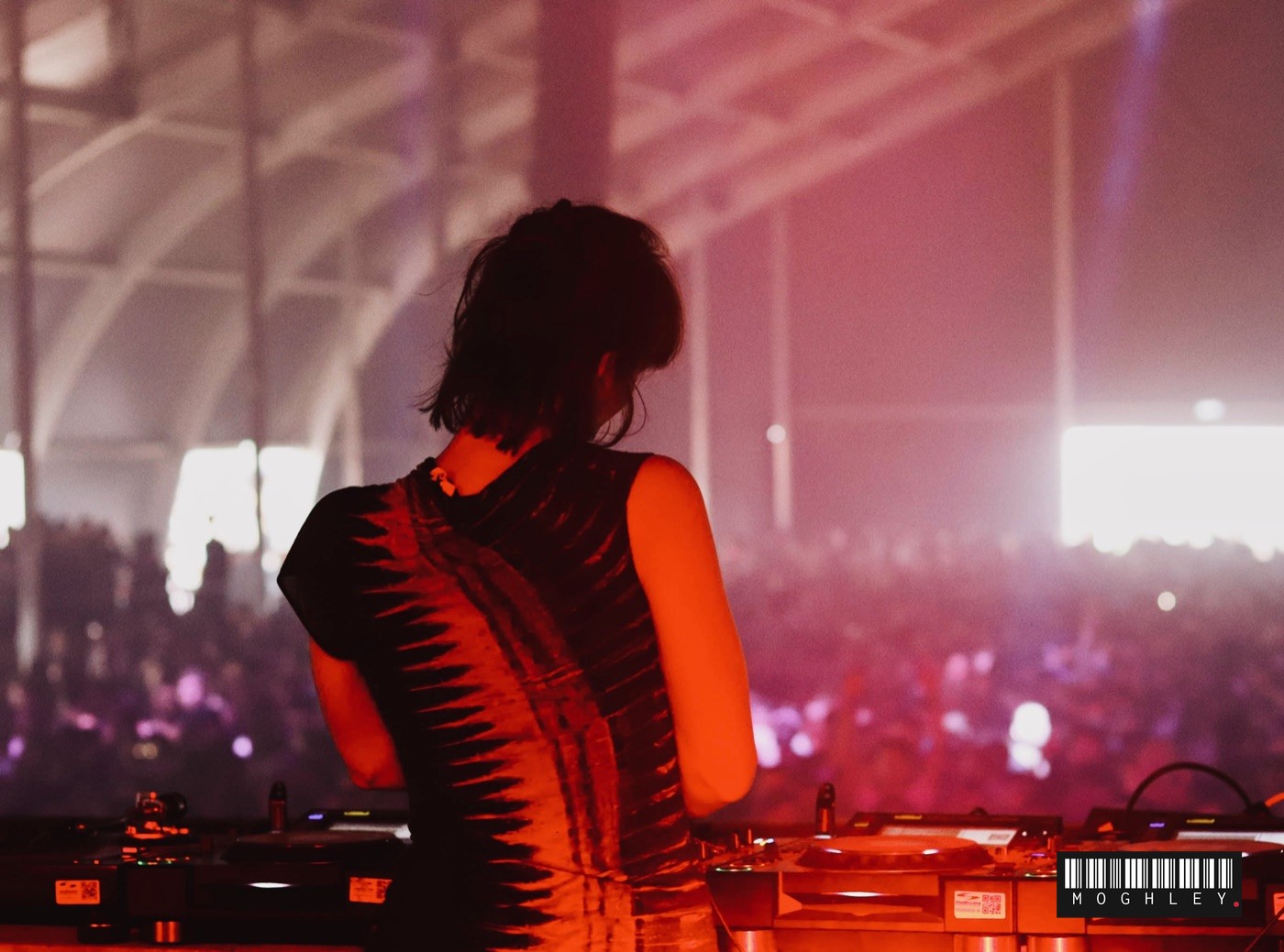 Performer facing a large festival crowd under a marquee, pink stage lighting