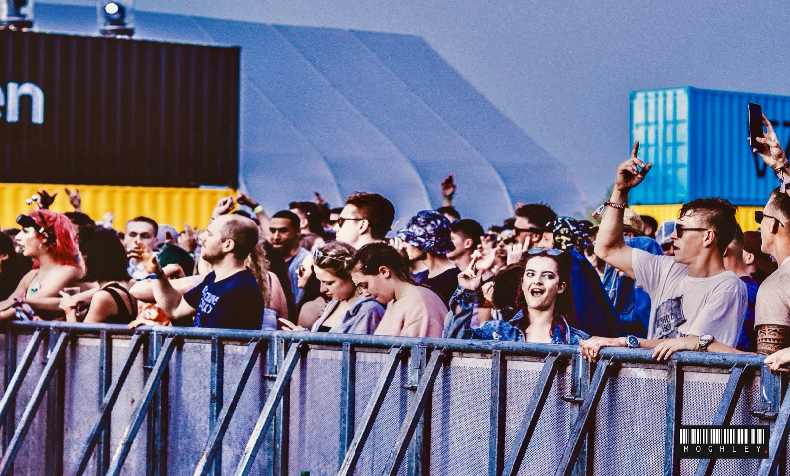 Crowd at a UK festival watching from behind a barrier, daytime