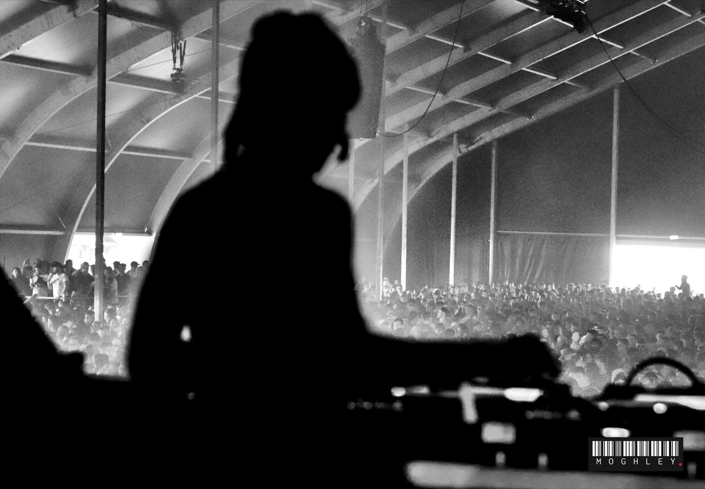 Black and white silhouette of a DJ performing under a marquee, facing the crowd