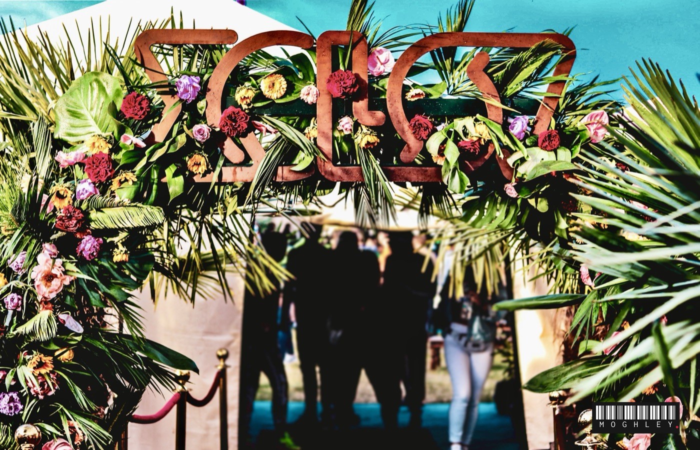 Festival entrance decorated with flowers, people walking through